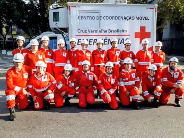 Equipe da filial, de uniforme e capacete, diante do Centro de Coordenação Móvel da Cruz Vermelha Brasileira